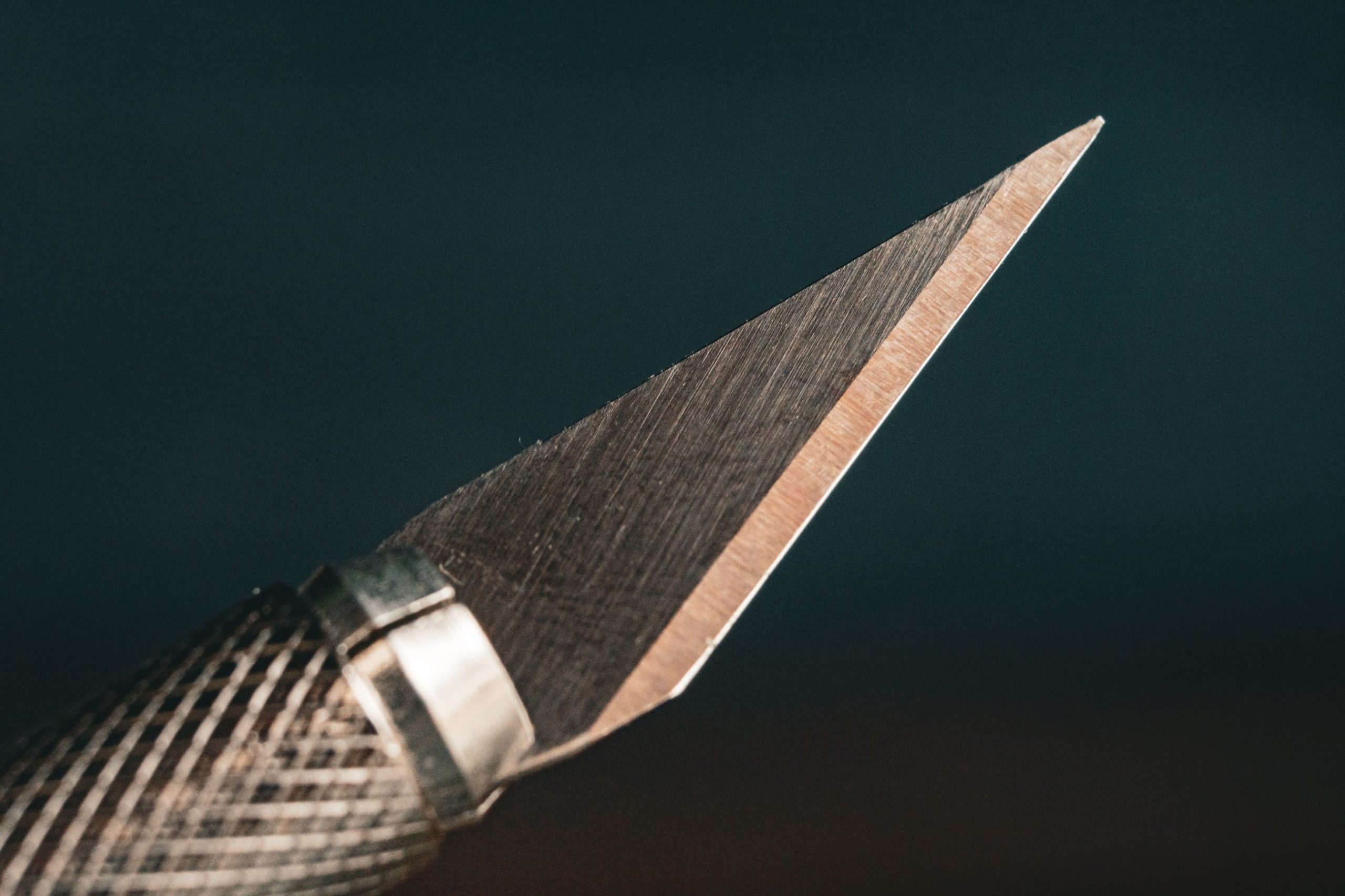 Close-up of a craft knife blade with a knurled handle on a dark background